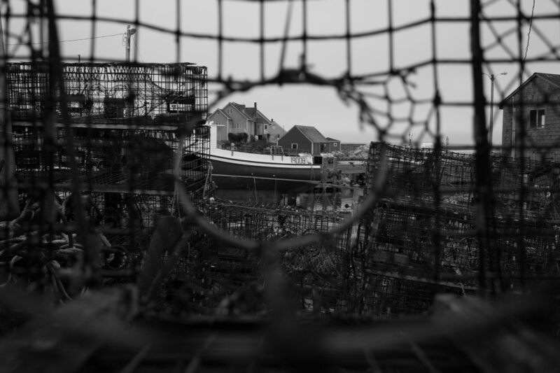 Der Blick aus einer Hummerfalle heraus auf Peggy's Cove und einem Fischerboot. Der Betrachter wird durch den "Rahmen" in die Bildmitte gelenkt.